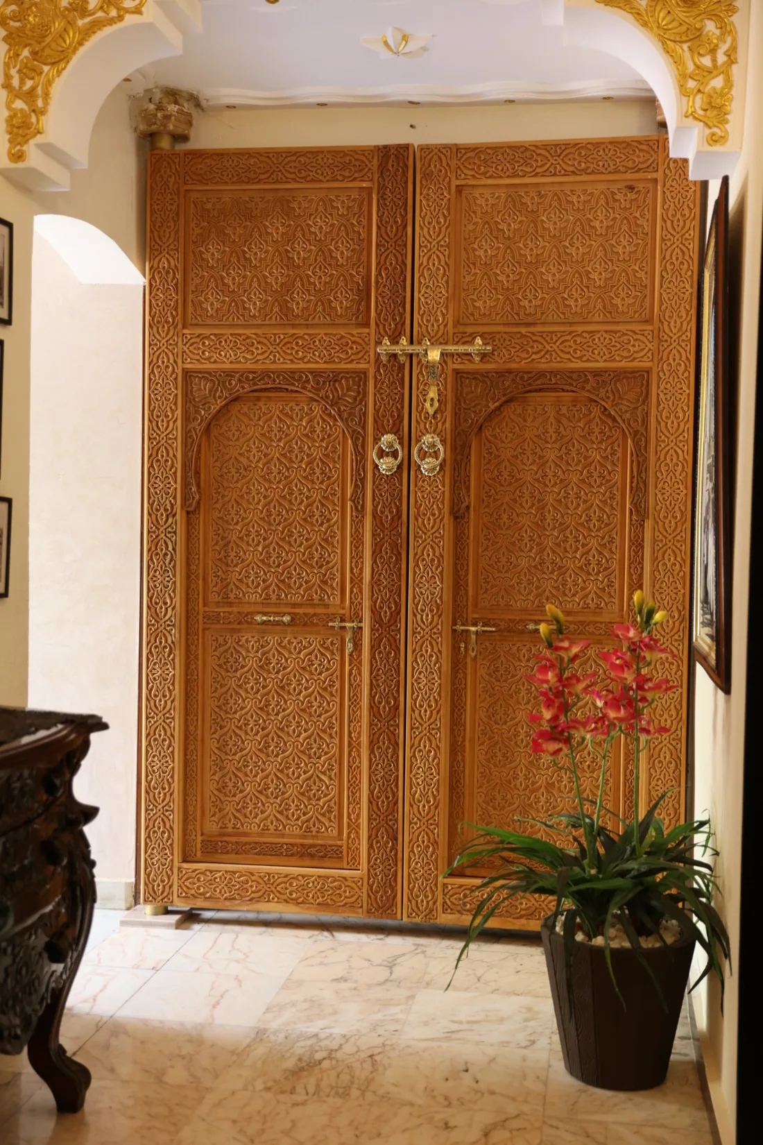 The carved cedar entrance door of Riad Sebti, with brass fittings and an orchid beside it.