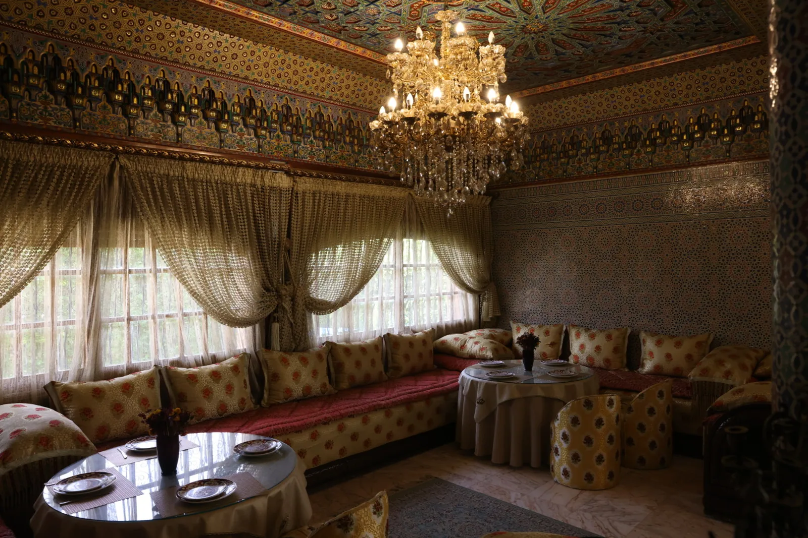 A Moroccan salon at Riad Sebti with carved plasterwork, chandelier and low banquettes.